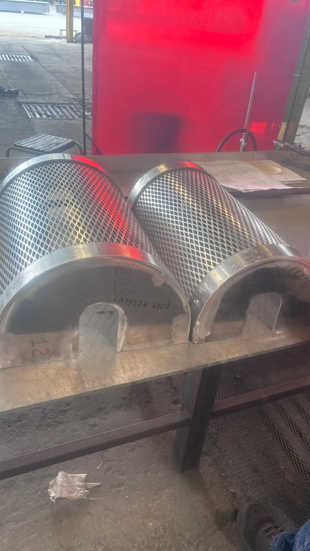 Two curved stainless mesh guards resting on a steel work bench